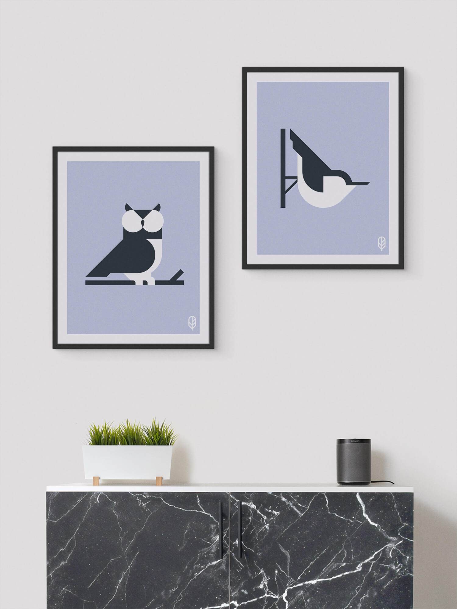 Two framed Flock Together prints displaying the illustrations of an owl and a nuthatch on the wall of a modern apartment