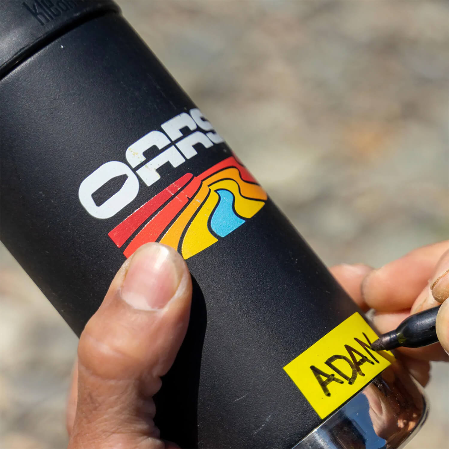 A hand labeling a black OARS water bottle on a river trip