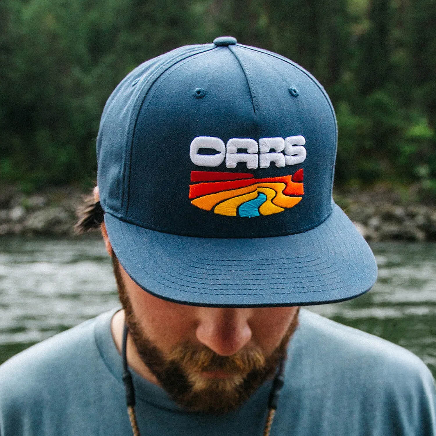 A person wearing a navy OARS cap beside a river