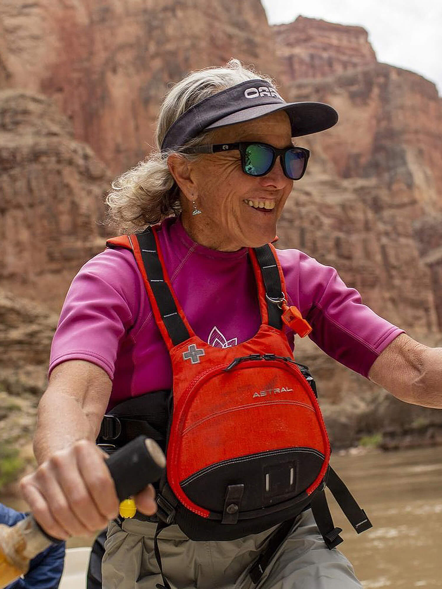 An OARS guide rowing a raft through a red-rock canyon